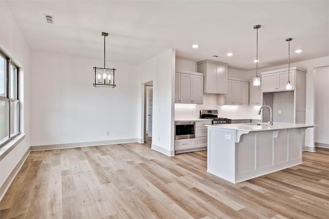 kitchen featuring built in microwave, an island with sink, pendant lighting, light hardwood / wood-style floors, and stainless steel stove