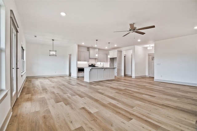 unfurnished living room with ceiling fan with notable chandelier, sink, and light hardwood / wood-style flooring