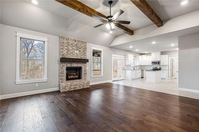 unfurnished living room featuring light wood-style flooring, a fireplace, a sink, a ceiling fan, and baseboards