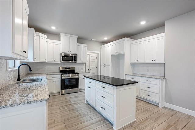 kitchen with tasteful backsplash, appliances with stainless steel finishes, light stone countertops, white cabinetry, and a sink