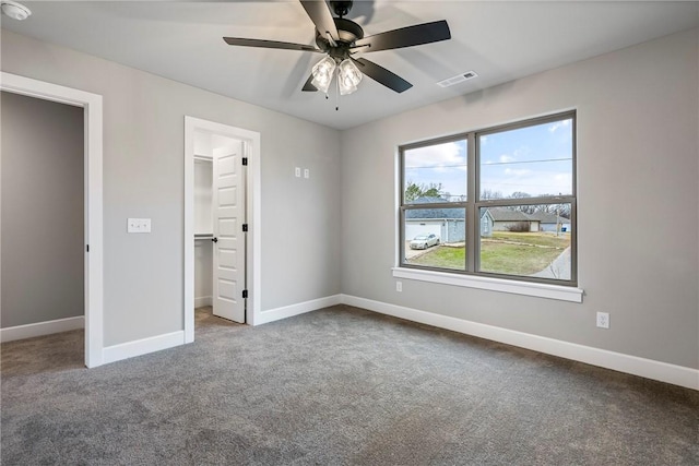 unfurnished bedroom featuring carpet, a walk in closet, visible vents, and baseboards