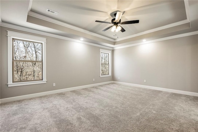 carpeted empty room with ceiling fan, visible vents, baseboards, a raised ceiling, and crown molding