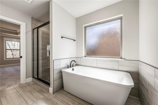 bathroom featuring a stall shower, a freestanding tub, tile walls, and a wainscoted wall