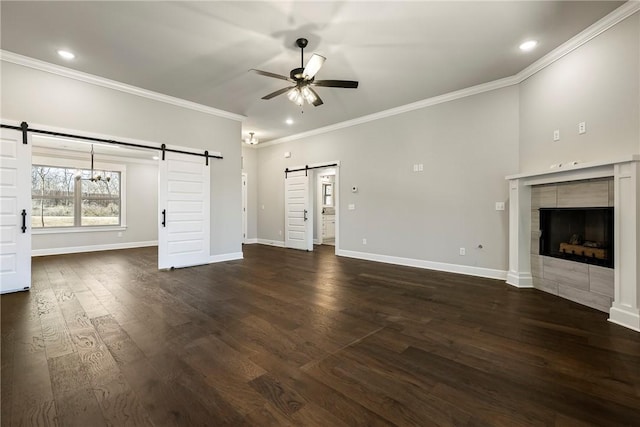 unfurnished living room featuring dark wood-style floors, a fireplace, a barn door, ceiling fan, and baseboards