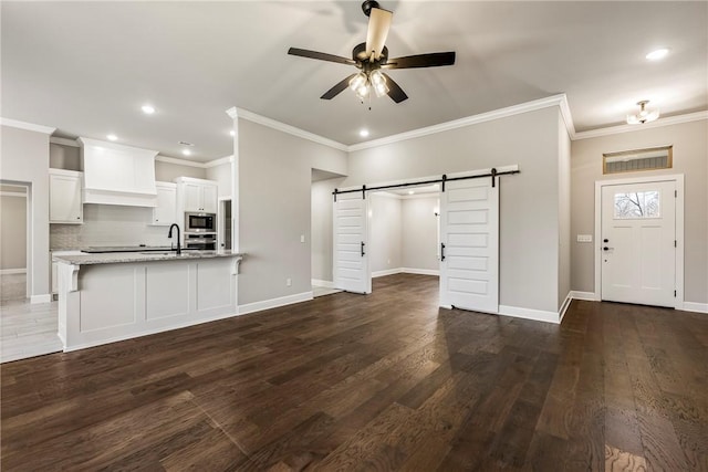 unfurnished living room featuring a barn door, dark wood-style flooring, a ceiling fan, and baseboards