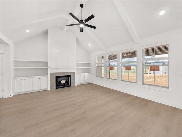 unfurnished living room with a wealth of natural light, a tiled fireplace, light wood-type flooring, and vaulted ceiling with beams