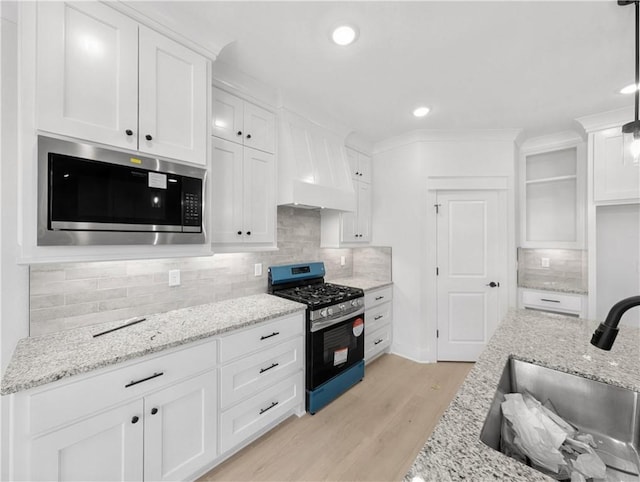 kitchen featuring tasteful backsplash, light wood-style flooring, appliances with stainless steel finishes, a sink, and white cabinetry