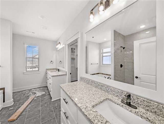 full bathroom with baseboards, tiled shower, two vanities, and a sink