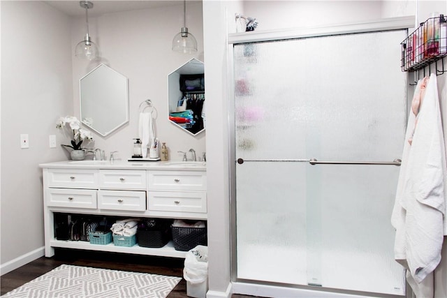 full bath with double vanity, a stall shower, baseboards, wood finished floors, and a sink