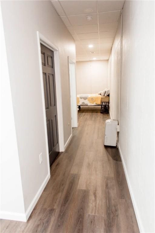 hallway featuring wood finished floors, a paneled ceiling, and baseboards