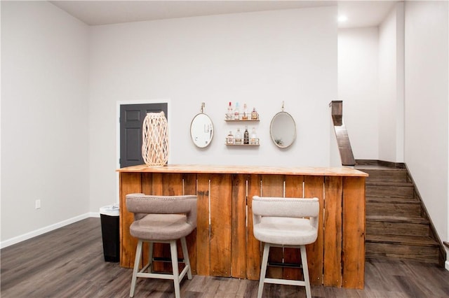 bar featuring dark wood-style floors, a bar, and baseboards