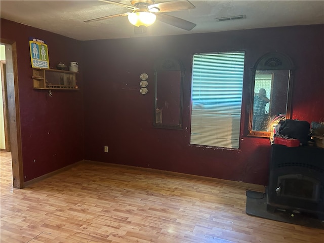 spare room with a wood stove, ceiling fan, and light hardwood / wood-style floors