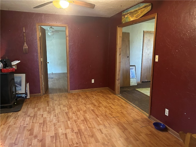 empty room featuring light wood-type flooring, a wood stove, and ceiling fan