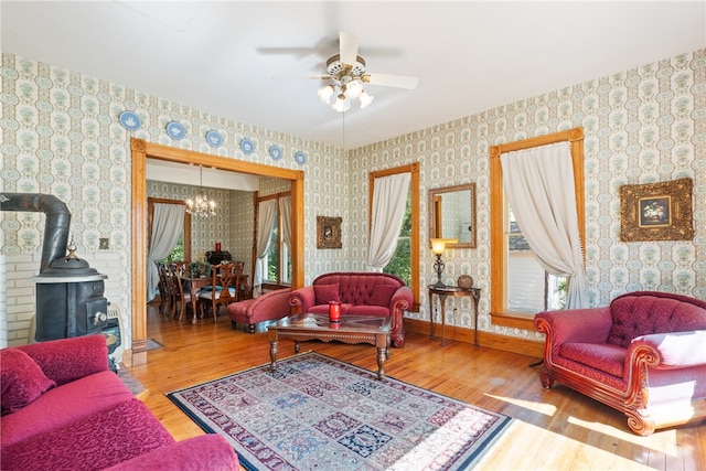 living room featuring a wood stove, wood-type flooring, and ceiling fan with notable chandelier