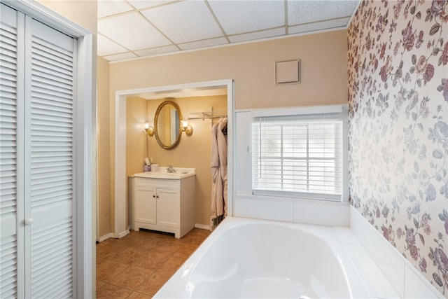 bathroom with a tub, a drop ceiling, vanity, and tile patterned floors