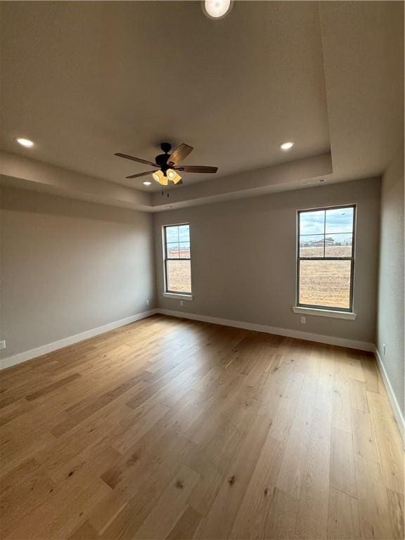 empty room with a raised ceiling, ceiling fan, and light wood-type flooring