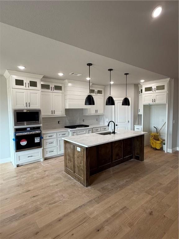 kitchen with appliances with stainless steel finishes, white cabinetry, sink, a kitchen island with sink, and light wood-type flooring