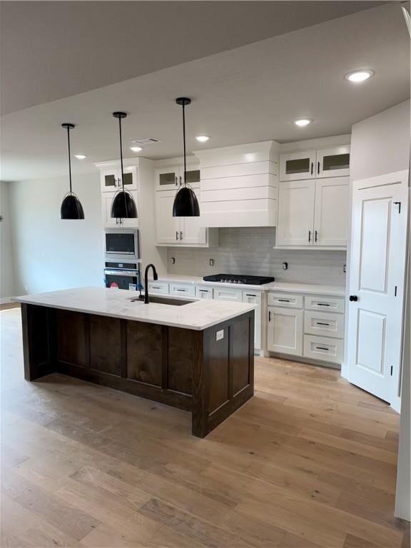 kitchen featuring white cabinetry, hanging light fixtures, a center island with sink, and appliances with stainless steel finishes