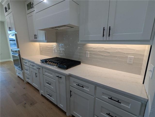 kitchen with white cabinetry, light hardwood / wood-style flooring, appliances with stainless steel finishes, light stone countertops, and backsplash