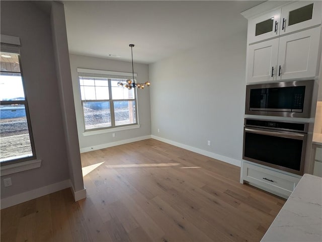 kitchen with white cabinetry, light hardwood / wood-style floors, stainless steel appliances, light stone countertops, and an inviting chandelier