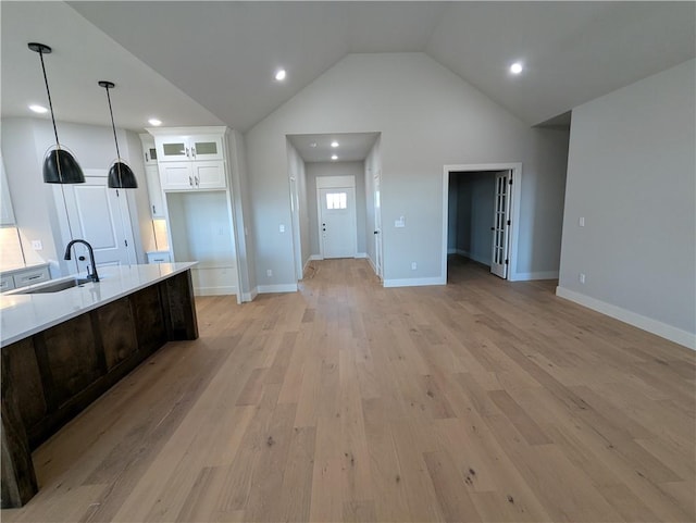 kitchen featuring sink, decorative light fixtures, high vaulted ceiling, light hardwood / wood-style flooring, and white cabinets