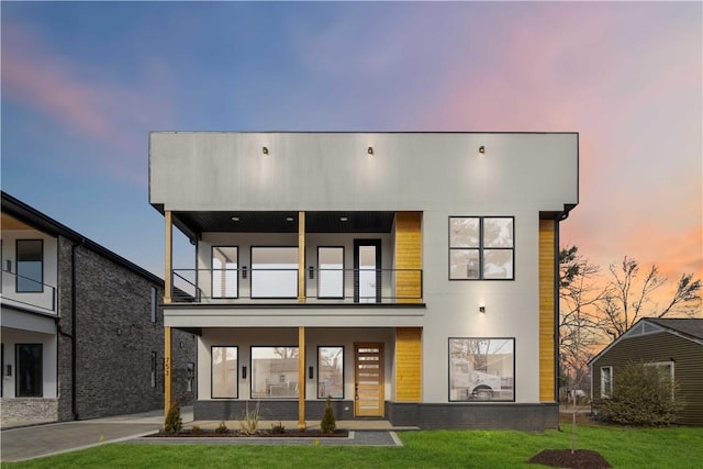 back house at dusk featuring a balcony and a yard