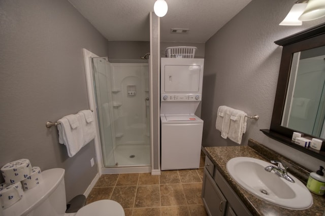 bathroom with vanity, stacked washing maching and dryer, a shower with shower door, a textured ceiling, and tile patterned flooring