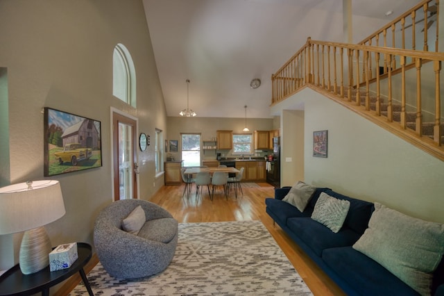 living room with an inviting chandelier, light hardwood / wood-style flooring, and high vaulted ceiling