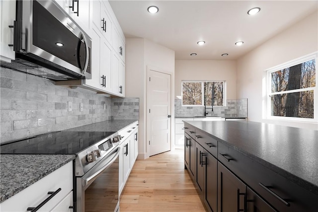 kitchen featuring light wood finished floors, dark stone countertops, stainless steel appliances, white cabinetry, and a sink