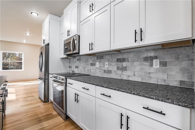 kitchen featuring decorative backsplash, dark stone countertops, stainless steel appliances, light wood-style floors, and white cabinetry