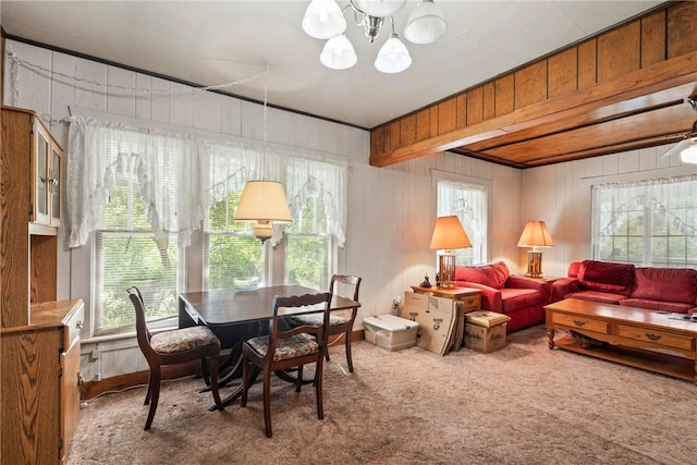 dining space with carpet flooring, a notable chandelier, a healthy amount of sunlight, and wooden walls