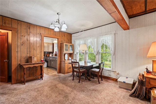 dining space with wood walls, beam ceiling, carpet floors, and an inviting chandelier