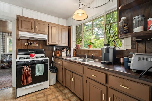 kitchen featuring white gas range oven, wood walls, and sink