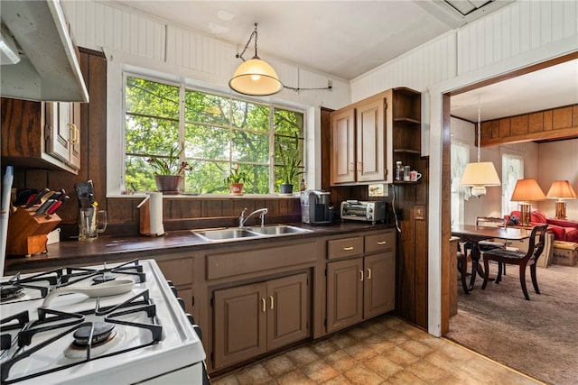 kitchen with white gas range, light colored carpet, sink, decorative light fixtures, and wood walls