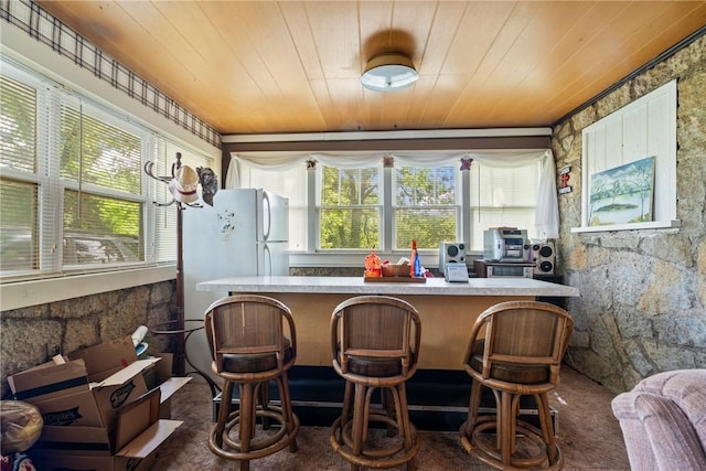 interior space featuring dark colored carpet, white fridge, wood ceiling, and a wealth of natural light