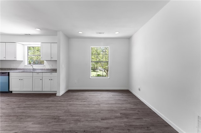 kitchen with stainless steel dishwasher, a wealth of natural light, dark wood-type flooring, and white cabinets