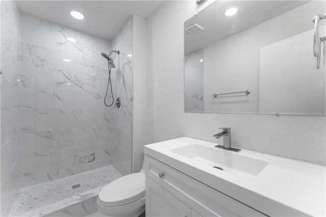 bathroom featuring a tile shower, vanity, and toilet