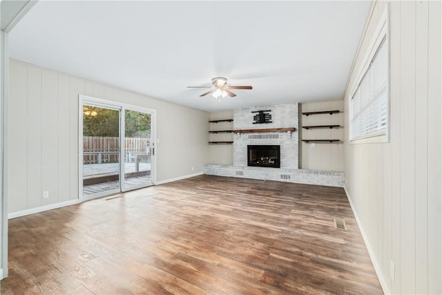 unfurnished living room with a fireplace, wood-type flooring, ceiling fan, and wood walls