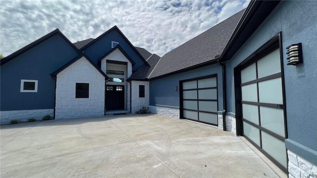 view of front facade featuring stucco siding, a shingled roof, concrete driveway, an attached garage, and stone siding