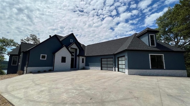 view of front of home featuring driveway, a shingled roof, stone siding, an attached garage, and stucco siding