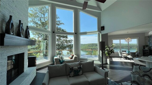 living room with a fireplace, a water view, ceiling fan with notable chandelier, and high vaulted ceiling