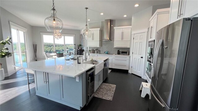 kitchen with a wealth of natural light, wall chimney range hood, stainless steel appliances, decorative backsplash, and a center island with sink