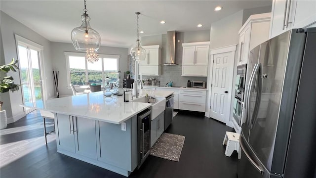 kitchen featuring white cabinets, appliances with stainless steel finishes, backsplash, wall chimney range hood, and a sink