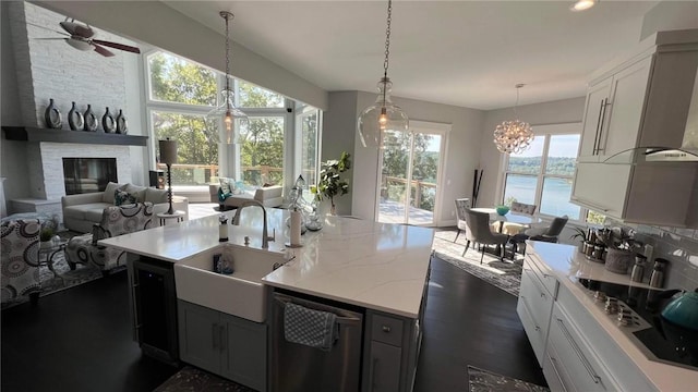 kitchen featuring a fireplace, a sink, an island with sink, dishwasher, and black electric cooktop