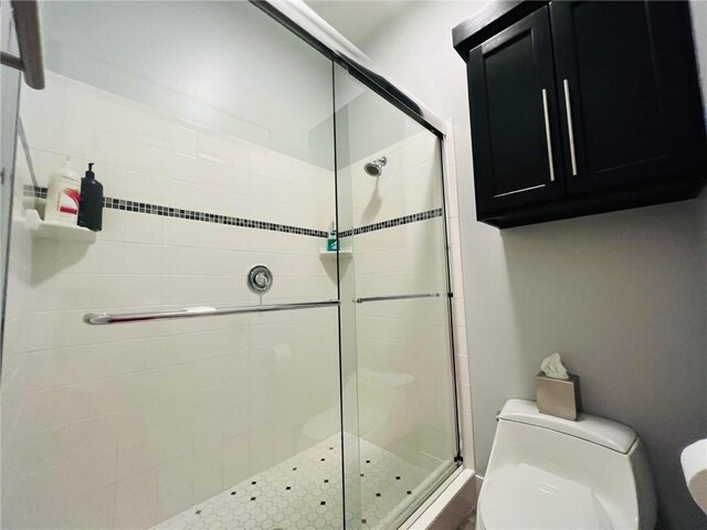 bathroom featuring a shower with door and toilet