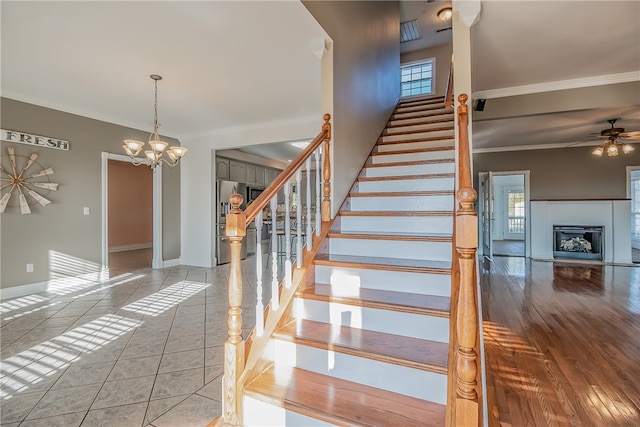 stairway with crown molding, ceiling fan with notable chandelier, and tile patterned floors