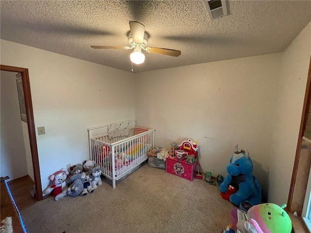 unfurnished bedroom featuring carpet floors, ceiling fan, a textured ceiling, and a nursery area