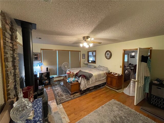 bedroom featuring a textured ceiling, ceiling fan, wood-type flooring, and a wood stove