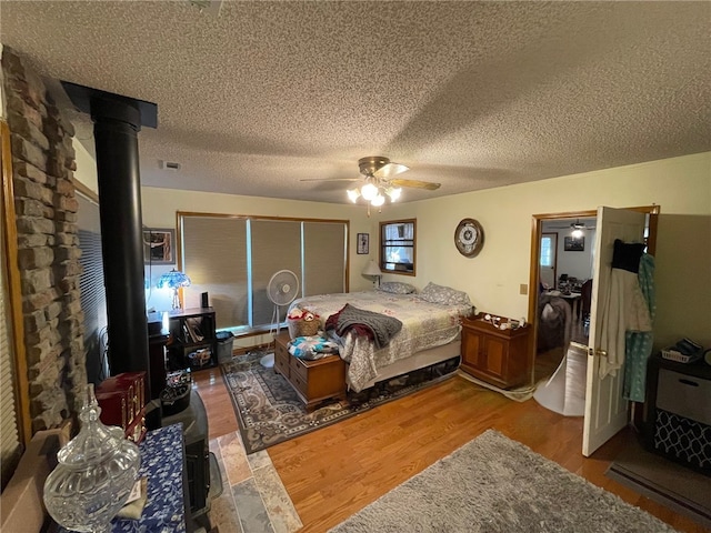 bedroom featuring ceiling fan, a wood stove, hardwood / wood-style floors, and a textured ceiling