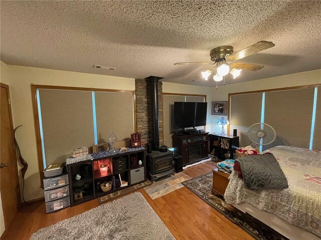 bedroom featuring a textured ceiling, a wood stove, wood-type flooring, and ceiling fan